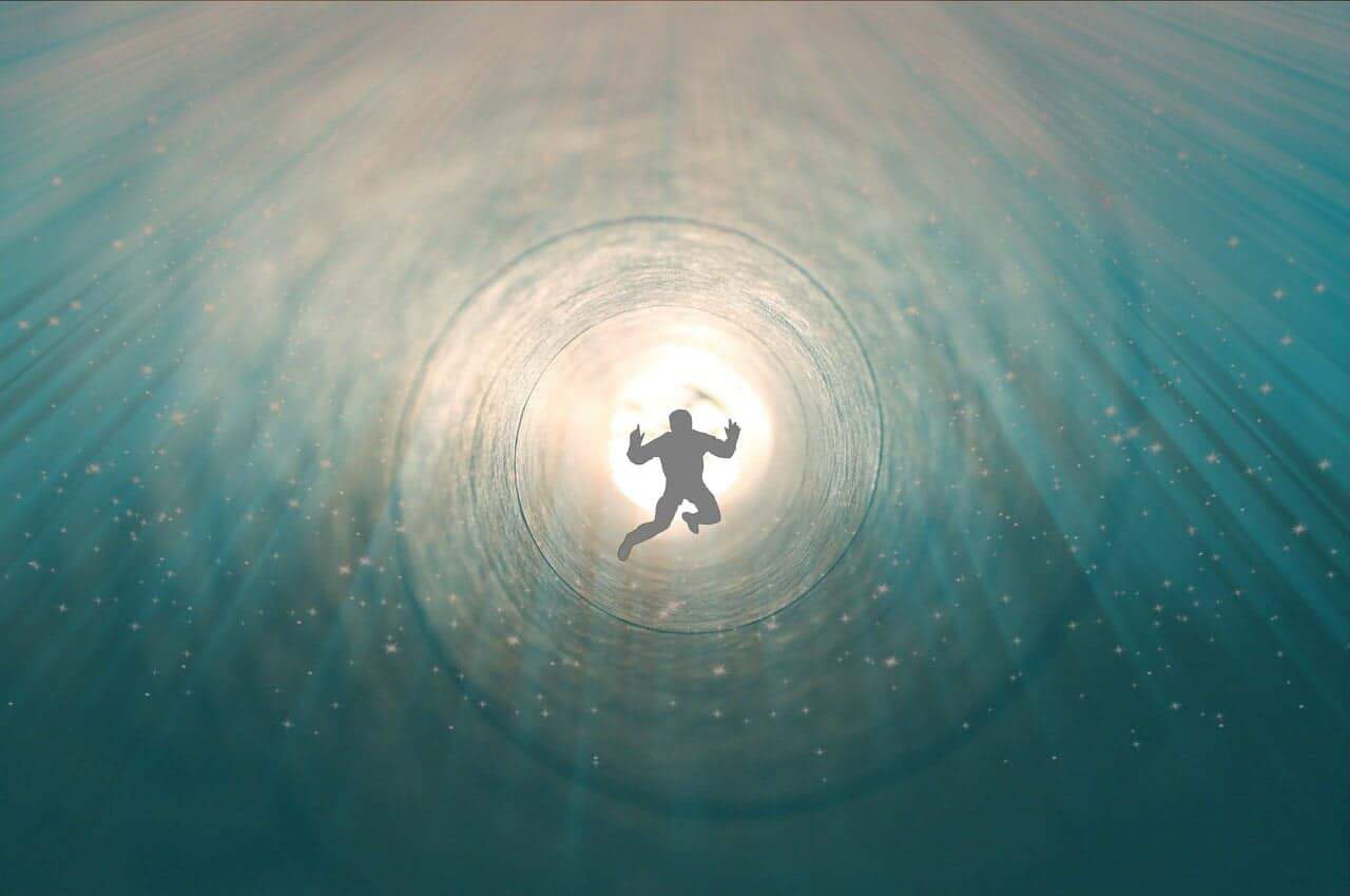 Person silhouetted against tunnel of light underwater.
