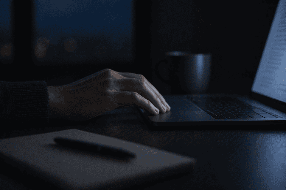 hand resting on laptop trackpad in low light with soft blue screen glow