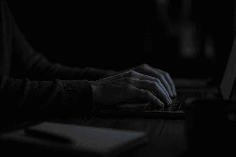 Close-up of hands typing on a keyboard in dim light, with surroundings fading into shadow